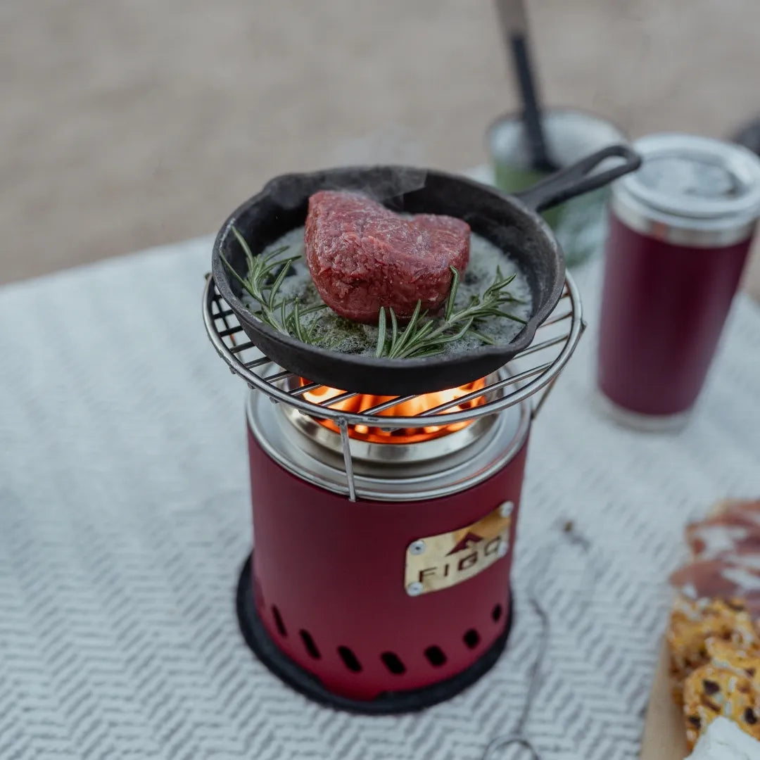 Red portable fire pit with a pan of meat and herbs on the grill