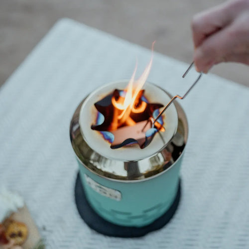 Person roasting a marshmallow over a portable FIGO Home fire pit with flames.
