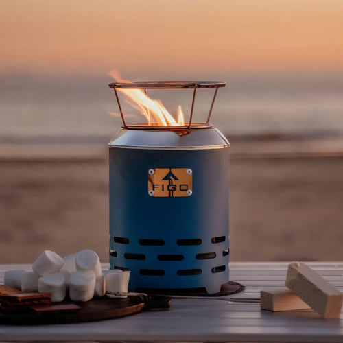Blue portable fire pit with flames on a wooden surface at sunset.