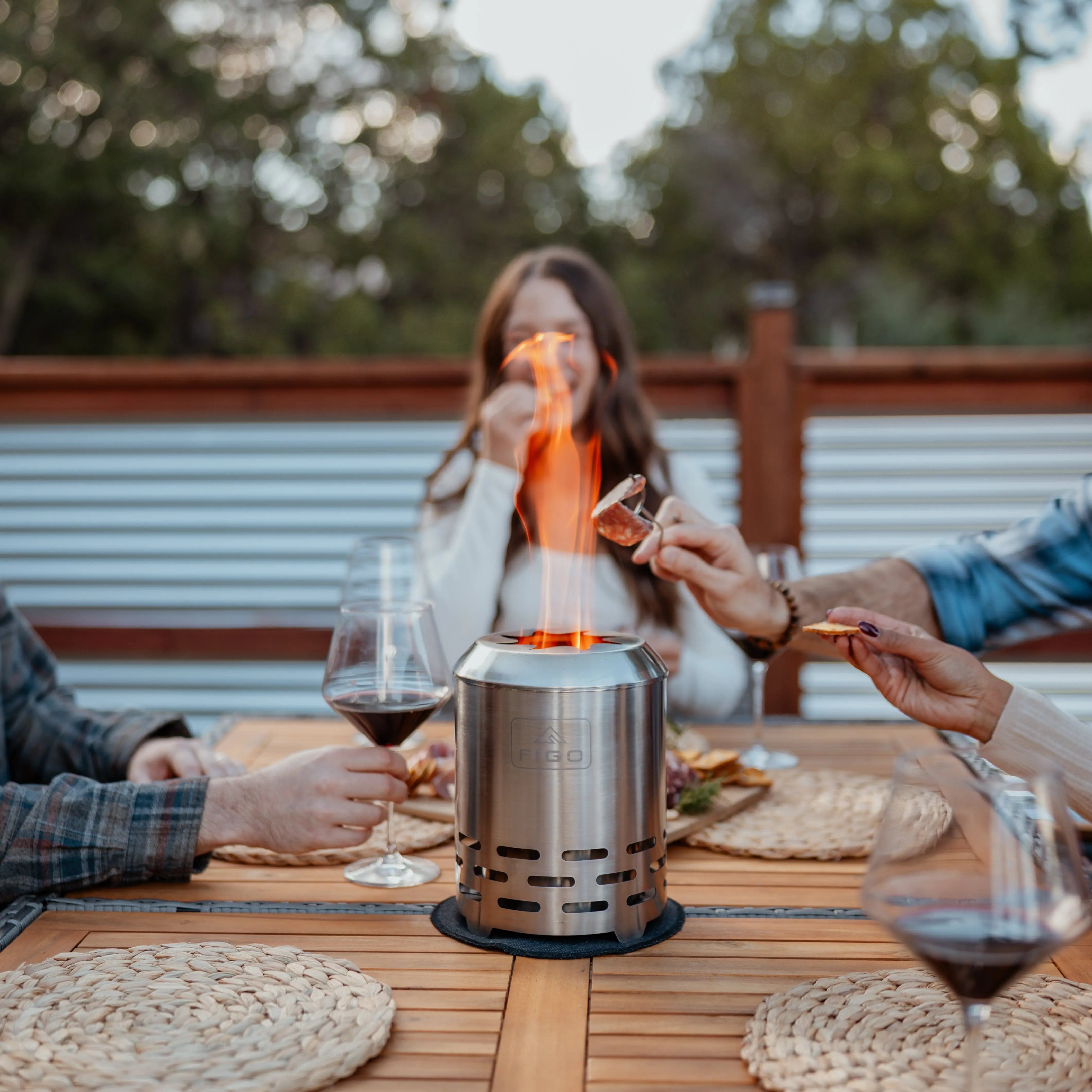 People around a table with a portable fire pit, enjoying a warm evening outdoors.